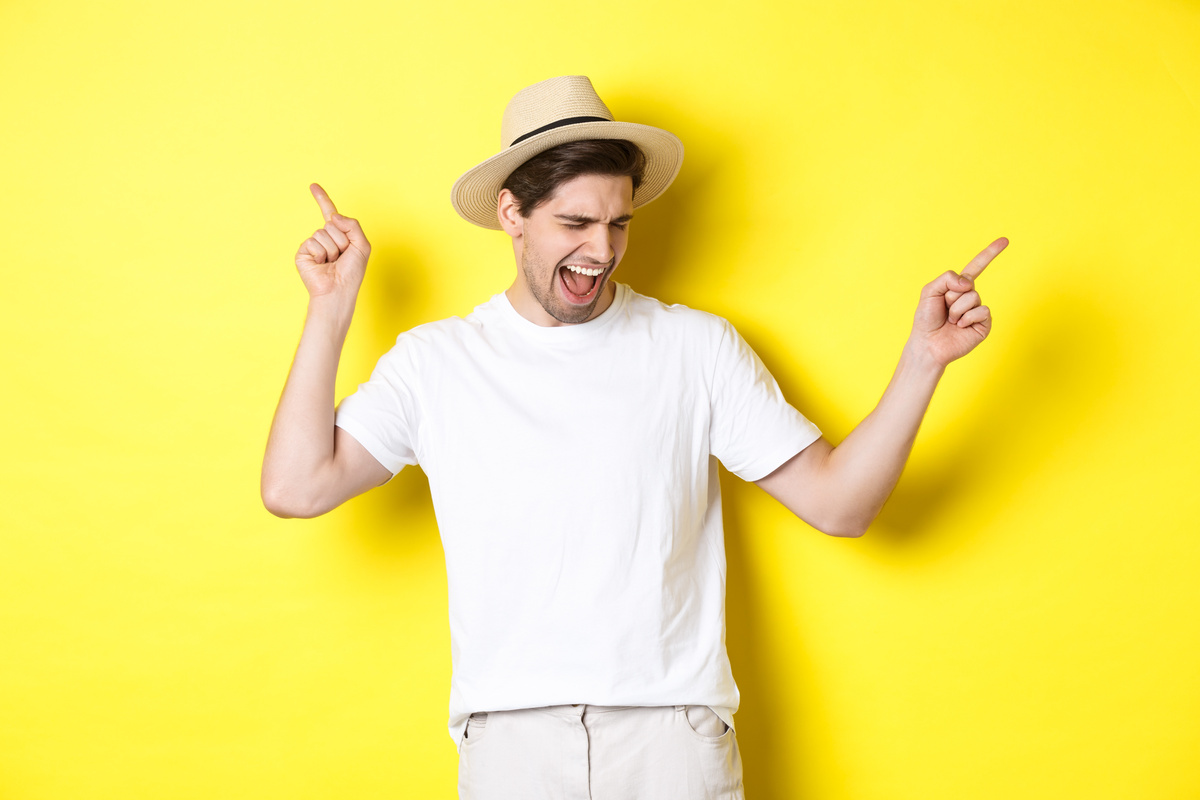 Concept of Tourism and Lifestyle. Happy Man Enjoying Vacation, Tourist Dancing over Yellow Background